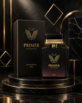 A 50ml bottle of PRIMÉR ESSENCE Eau de Parfum next to its black packaging box, both featuring gold lettering and a gold leaf emblem, displayed on a black marble pedestal with gold geometric accents.